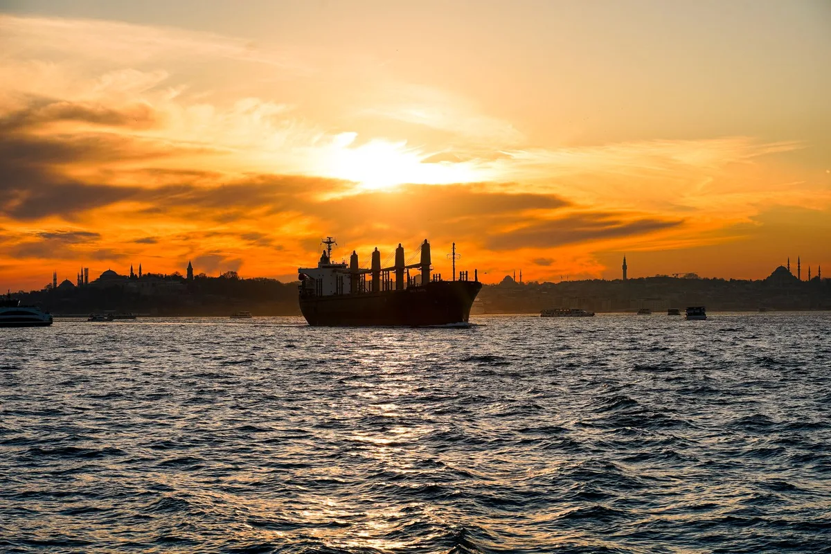 Cargo ship crossing a narrow strait at sunset near Bab el Mandeb.