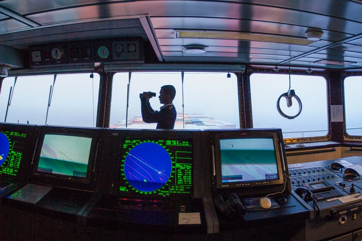 Merchant navy officer using binoculars on a ship bridge, merchant navy qualifications guide.